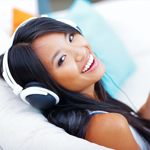 A woman sitting back on couch with headphones on her head and smiling.