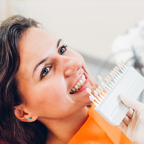 A patient smiling as a dentist compares a row of veneers to her teeth