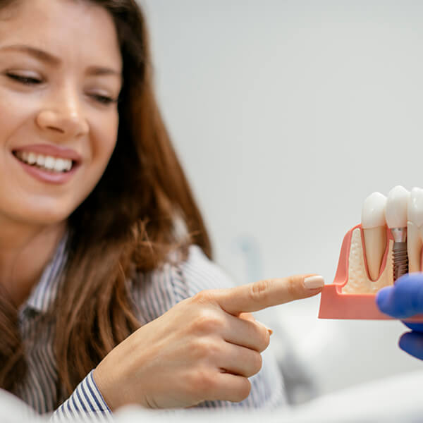 A patient pointing to a dental implant model